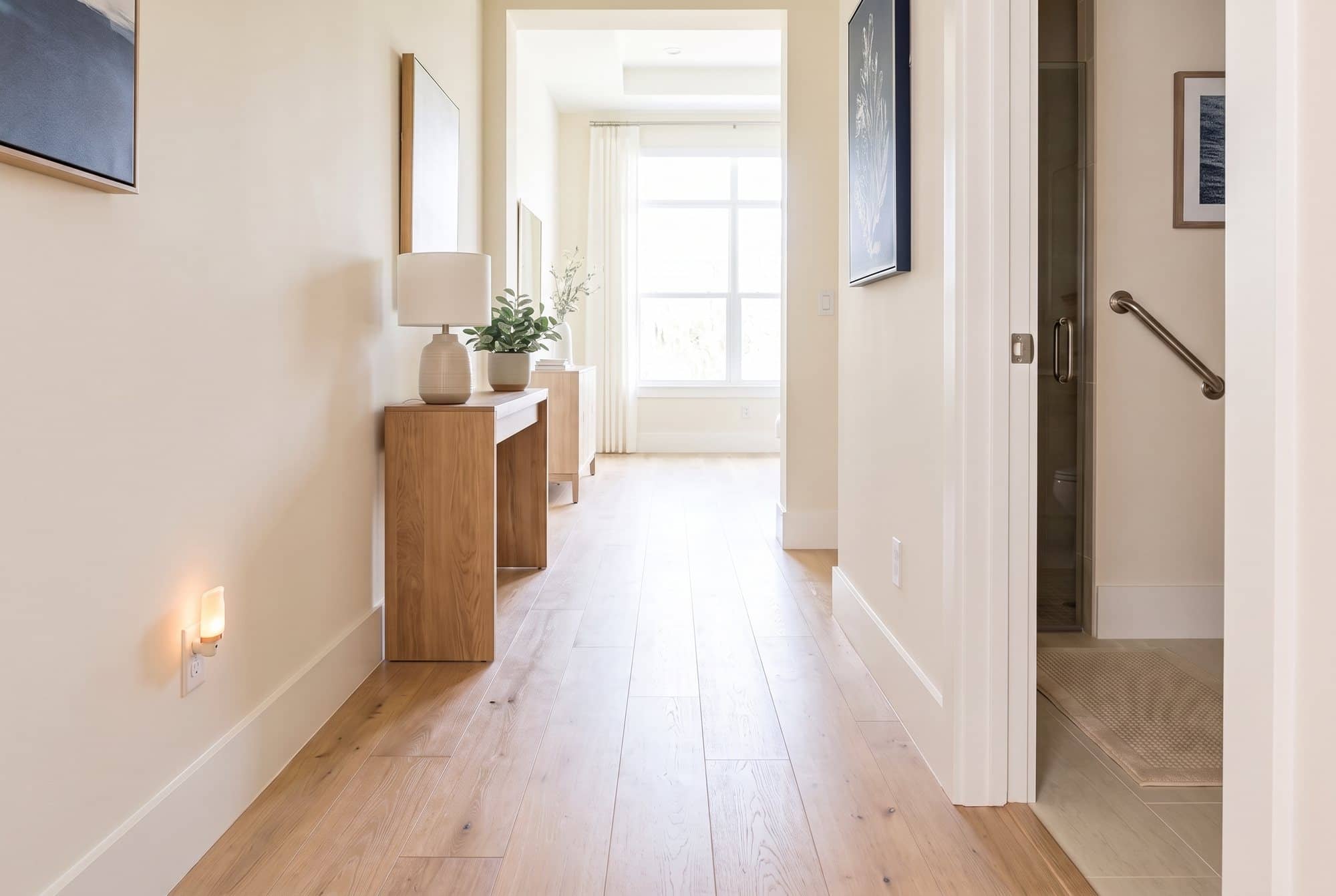 A tidy, well-lit hallway with a glowing night-light, a clear oak floor and a grab bar inside the bathroom door