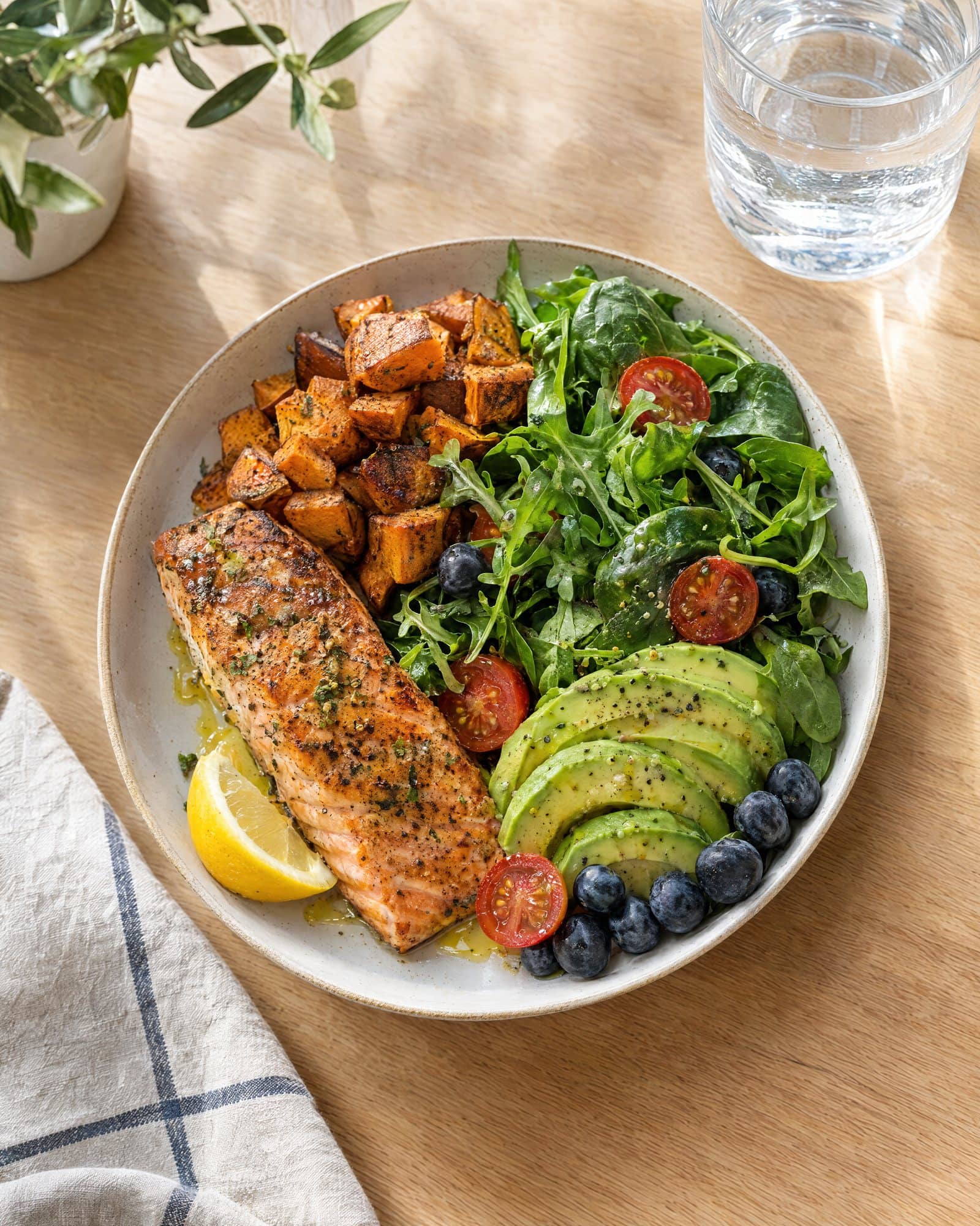 A balanced plate of salmon, sweet potato, greens, avocado and berries